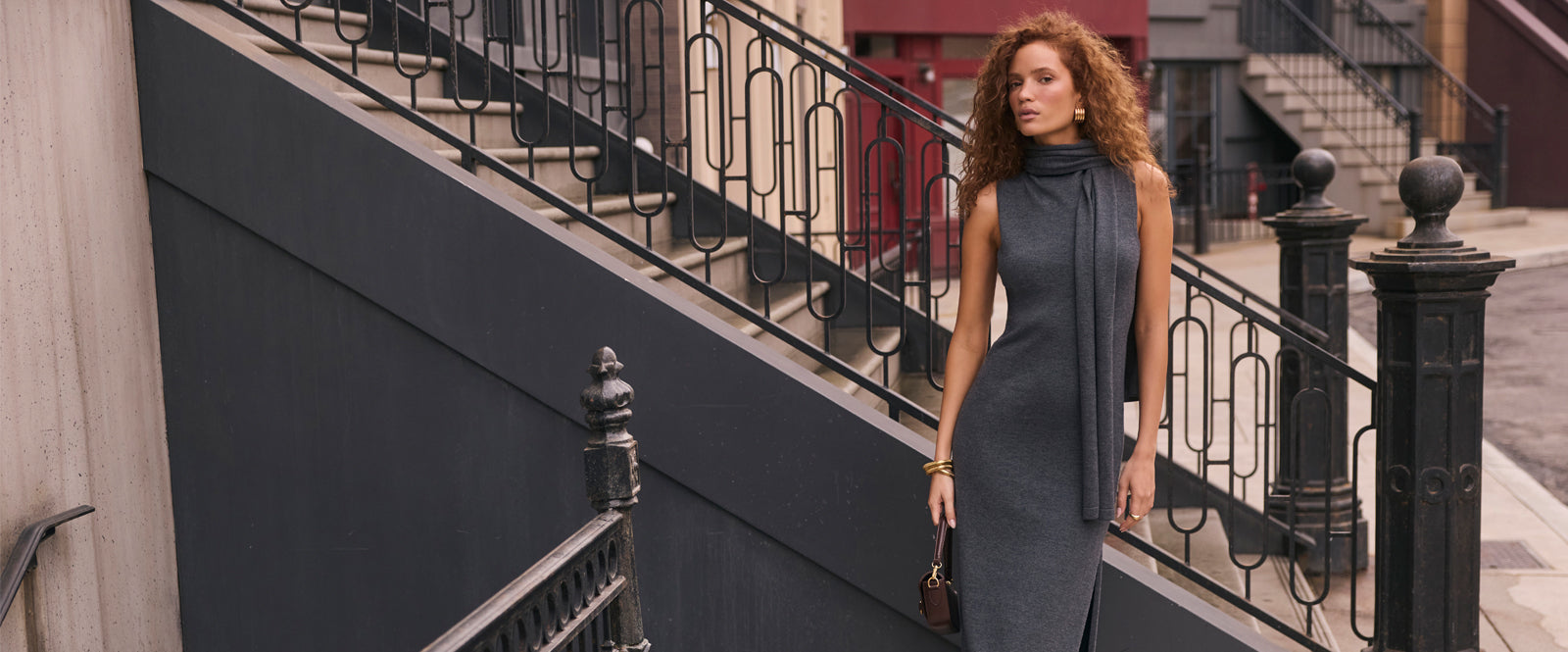 Woman in a sleeveless, fitted gray turtleneck dress with black side panels and holding a dark handbag.