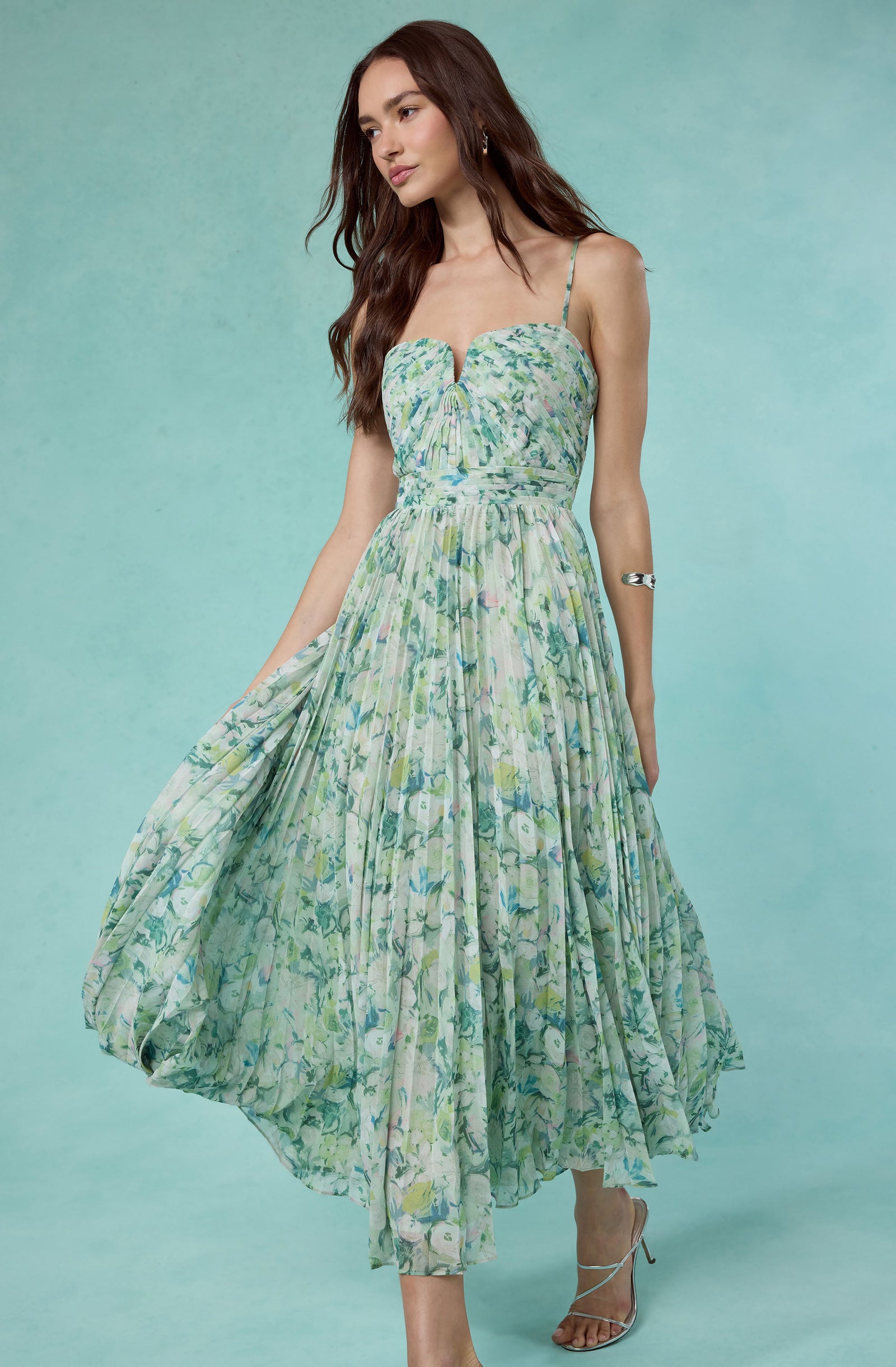 Woman in a green floral maxi dress with spaghetti straps and a pleated skirt.