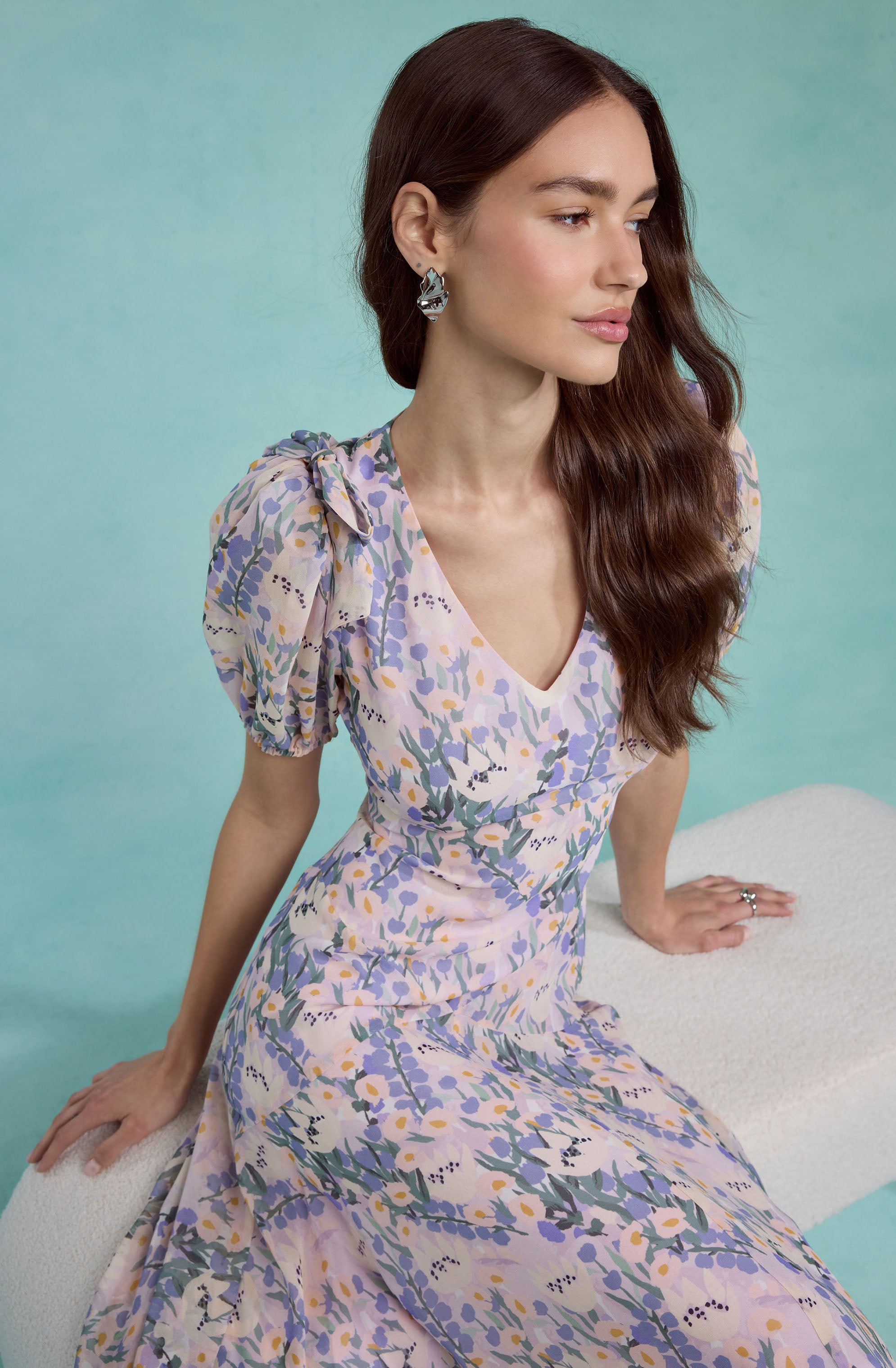 Woman in a pastel floral dress with puff sleeves, sitting on a white bench.
