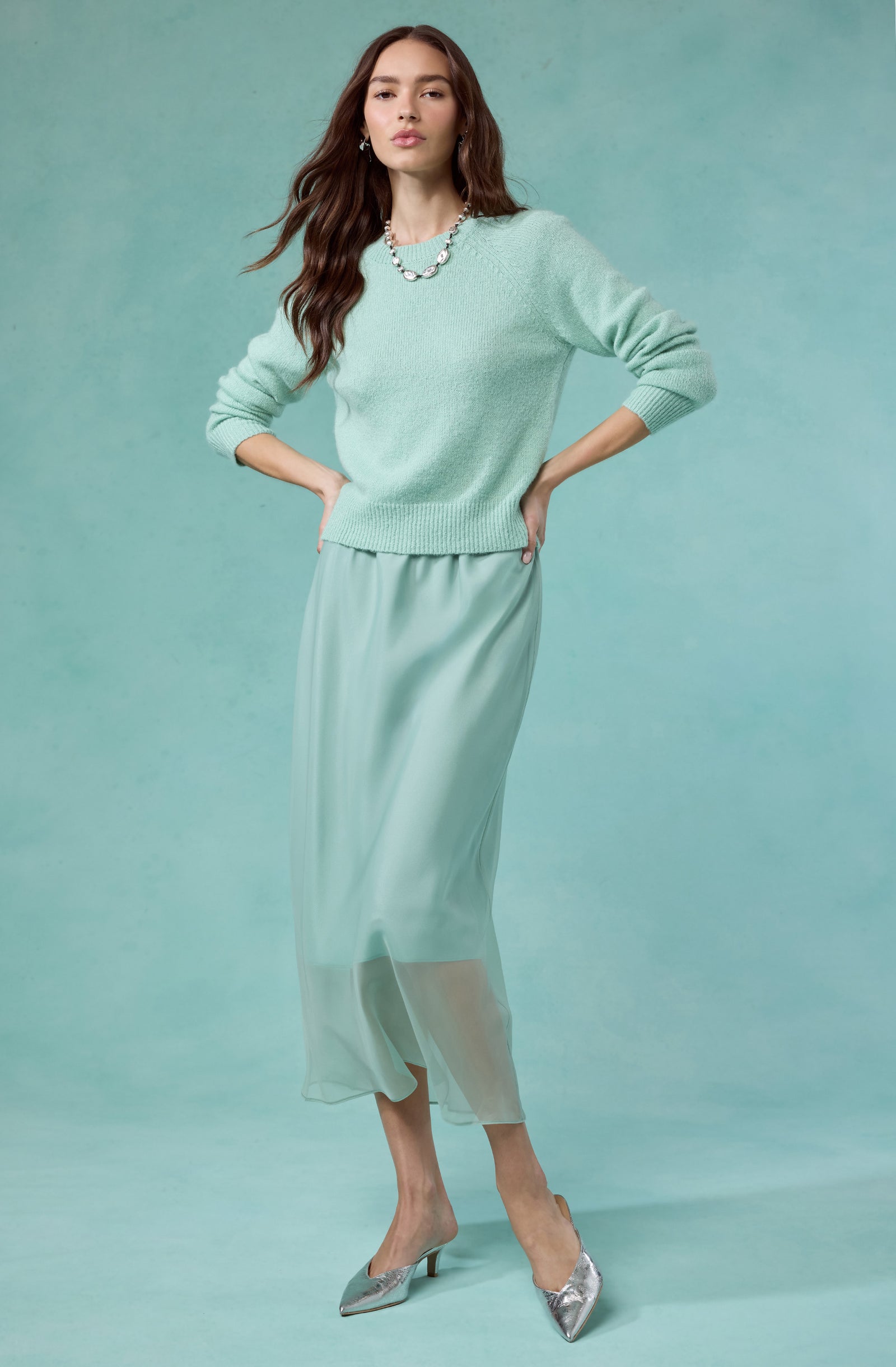 Woman wearing a mint green sweater, matching sheer skirt, and silver heels.