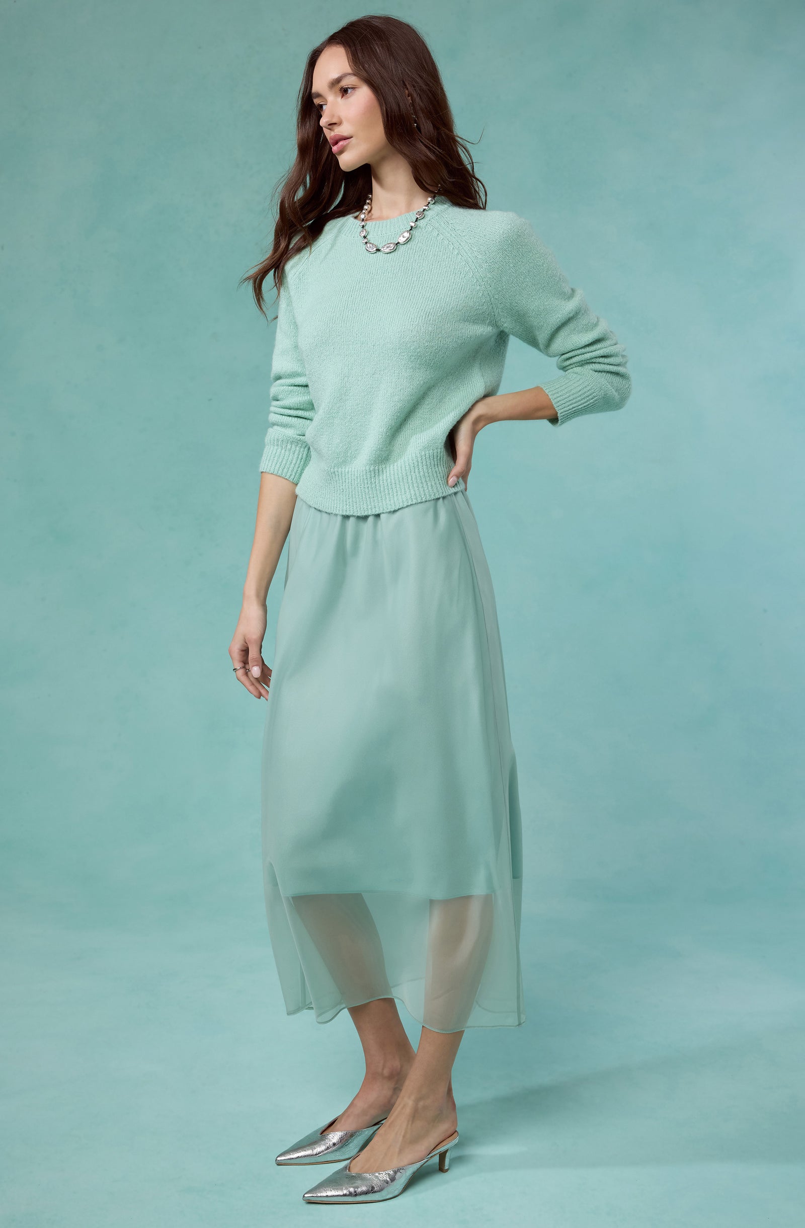 Woman wearing a mint green sweater, matching sheer midi skirt, and silver heels.