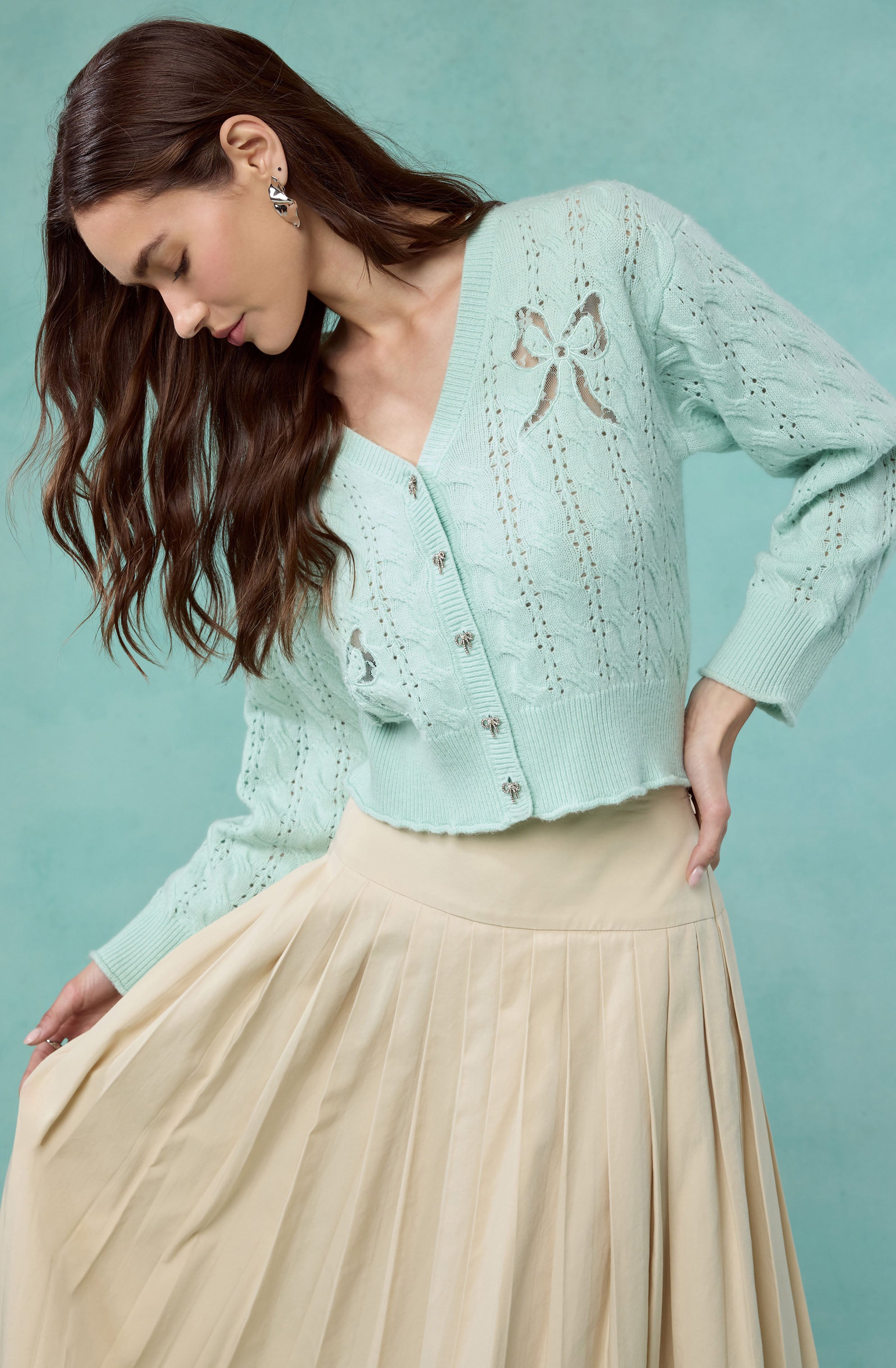 Light blue knit cardigan with bow cutouts and a pleated beige skirt.