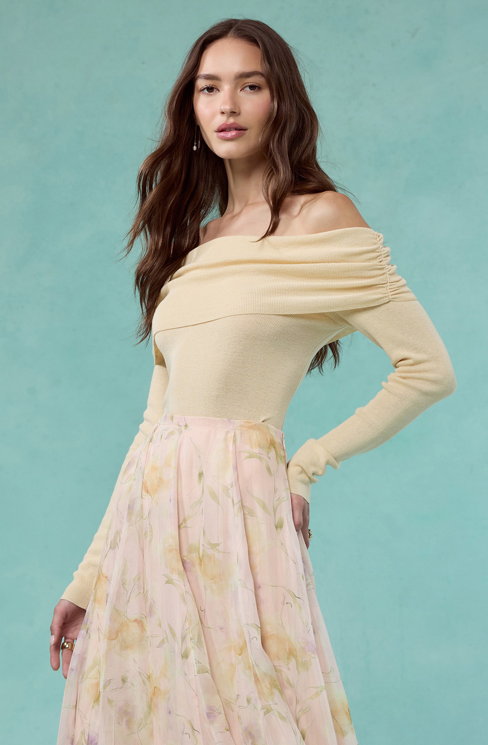 Woman wearing a cream off-the-shoulder sweater and a pastel floral skirt.