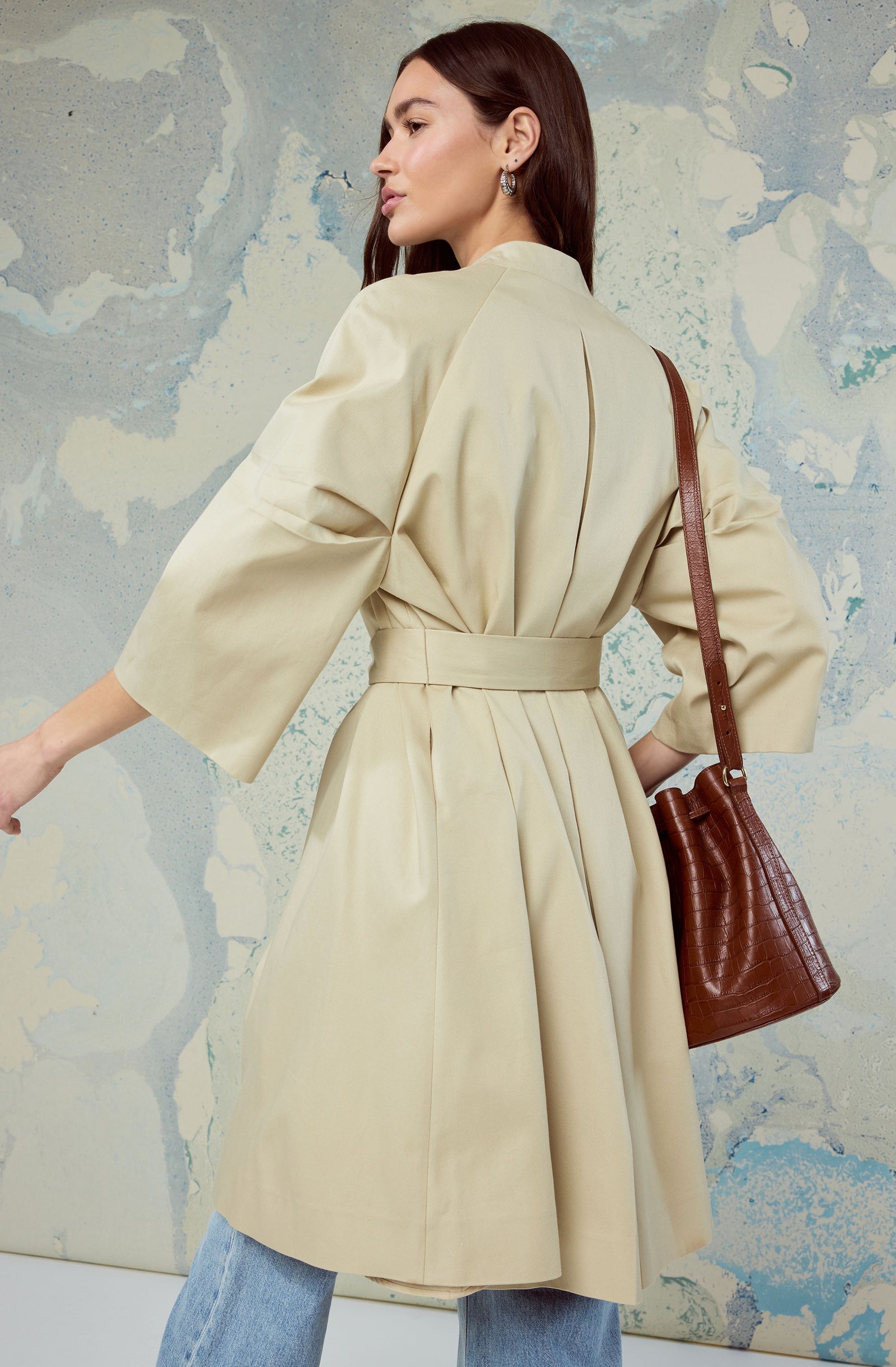 Woman in a cream trench coat with puffed sleeves, carrying a brown leather handbag.