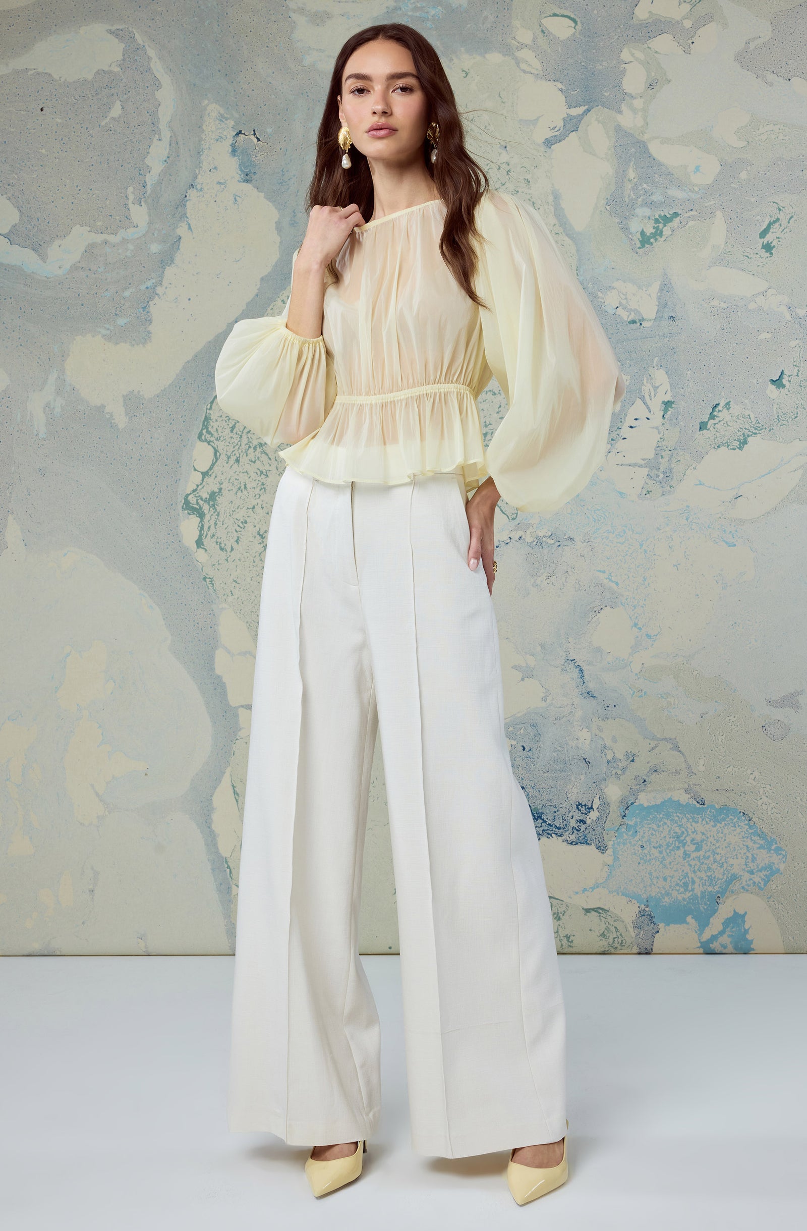 Woman wearing a cream sheer puff-sleeve blouse and high-waisted white wide-leg pants.