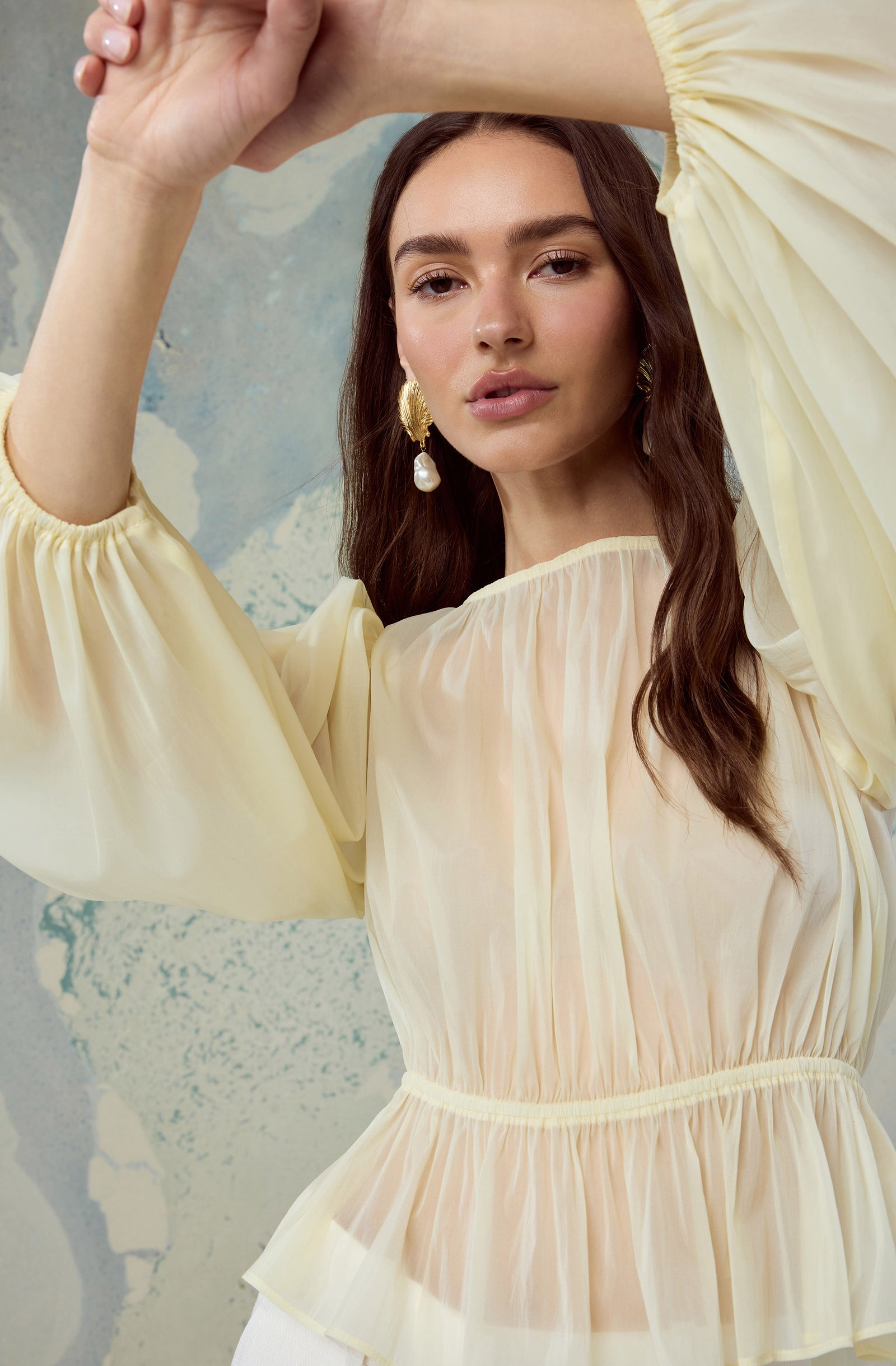 Woman in a light yellow, long-sleeve, pleated dress with puffed sleeves and gathered waist.