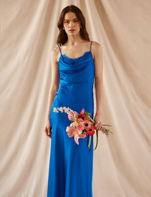Woman in a blue satin slip dress with lace trim, holding a bouquet of pink and red flowers.