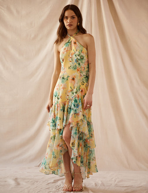 Woman in a sleeveless, floral, tiered maxi dress with ruffles and a front slit.