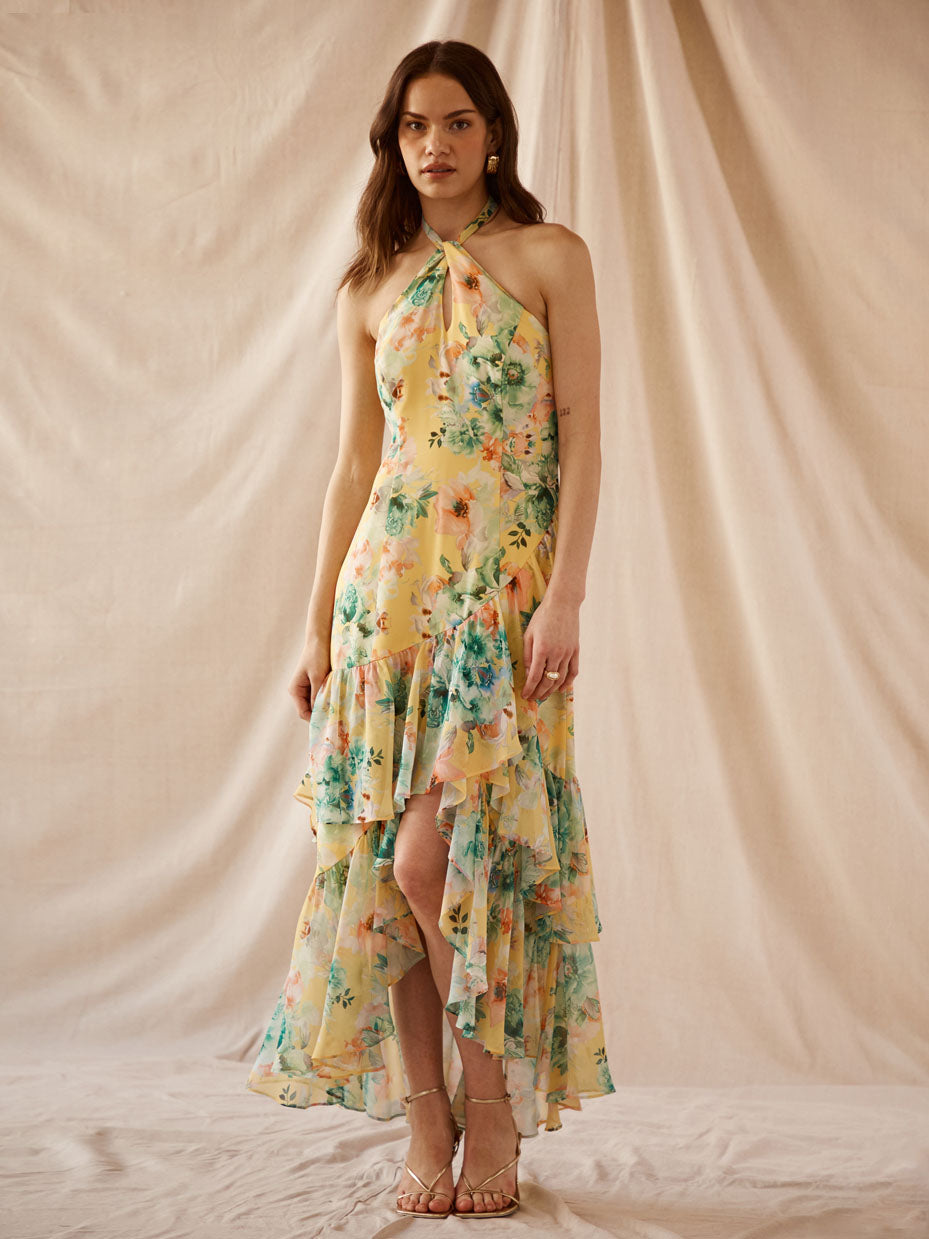 Woman wearing a yellow floral halter dress with ruffles and a slit.