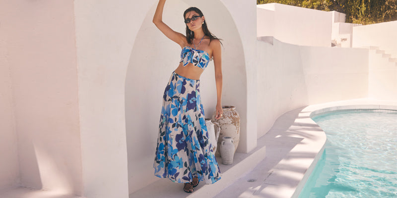 Woman in a blue floral crop top and matching high-waisted, flowy skirt by a pool.