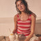 Woman in a red and white striped tank top and beige ruffled skirt holding a coconut drink.