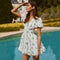 Woman in a white dress with blue floral prints, puff sleeves, and a fitted waist.