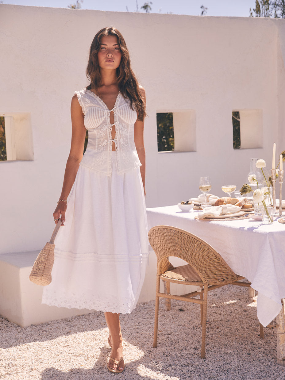 Woman in a white sleeveless handkerchief dress with lace details and eyelet embroidery.