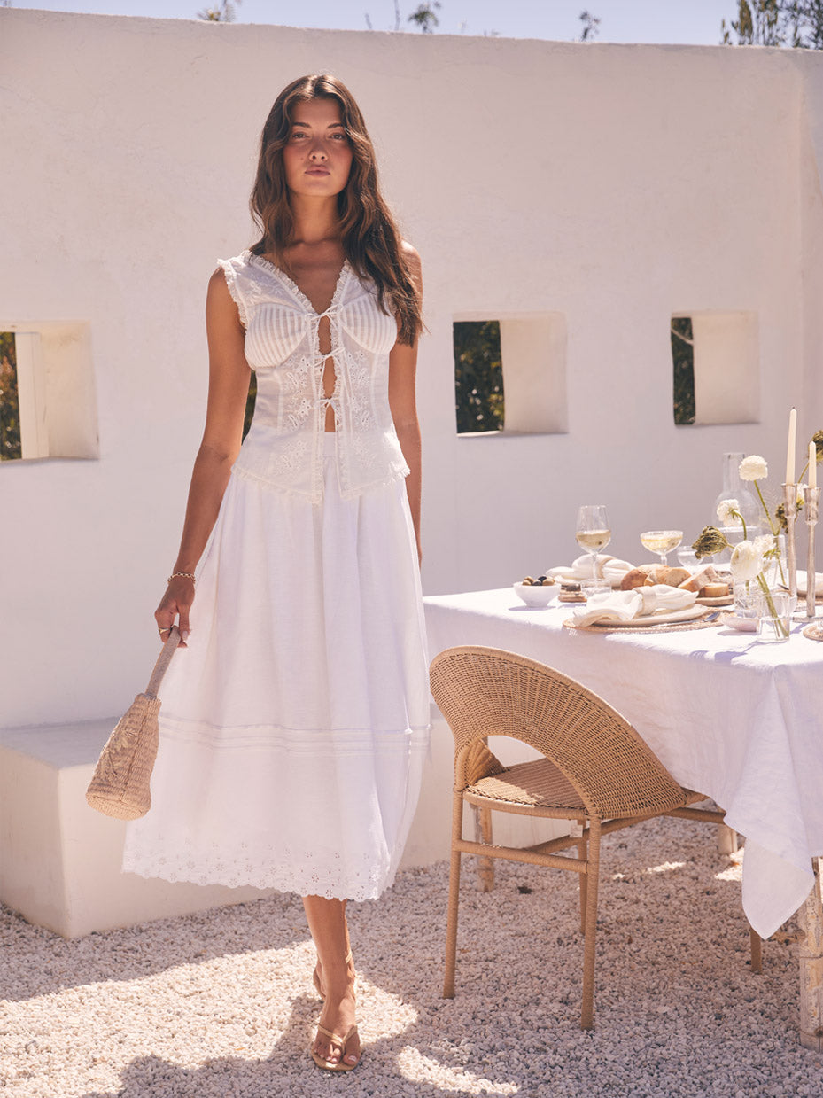 Woman wearing a sleeveless white dress with lace details and a long, flowy skirt.