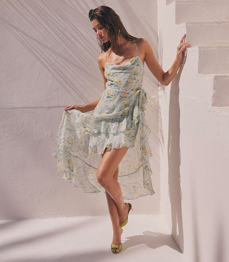Woman wearing a flowy, pastel floral dress with thin straps and ruffled hem.