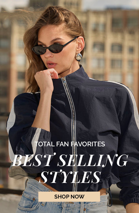 Woman wearing a navy windbreaker jacket with white stripes on the sleeves and high-waisted jeans.