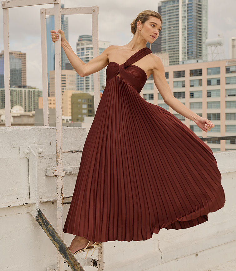 Woman in a one-shoulder, pleated, floor-length burgundy dress on a rooftop.