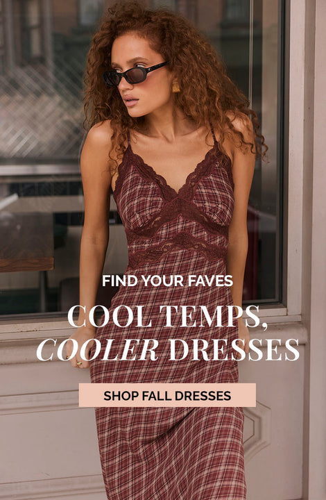 Woman in a plaid dress with lace, wearing sunglasses, standing indoors near a window.