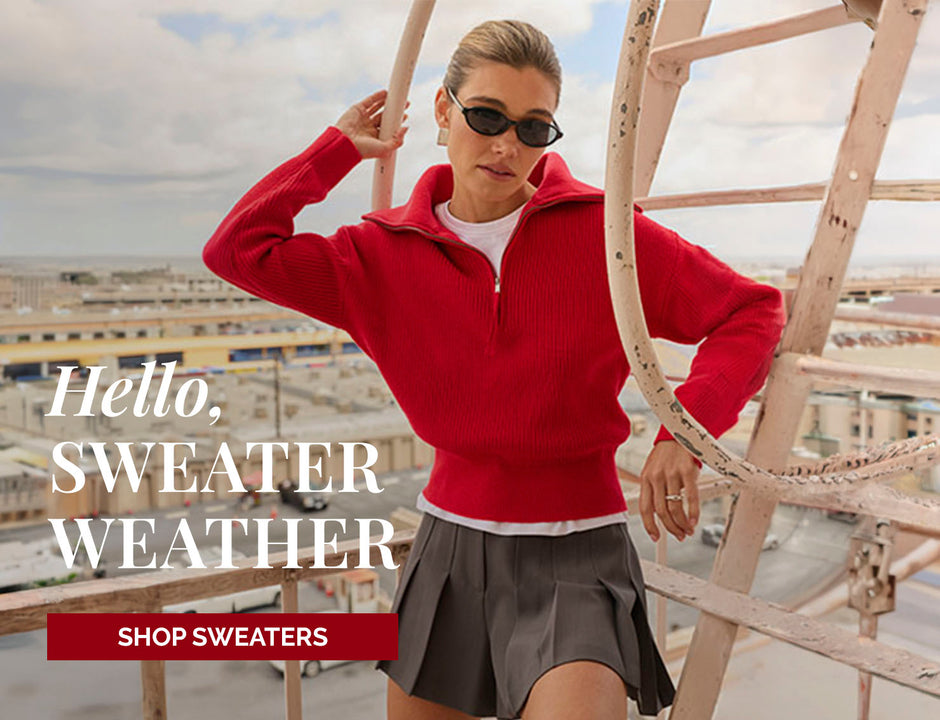Woman in a red zip-up sweater, gray pleated skirt, and sunglasses on rooftop.