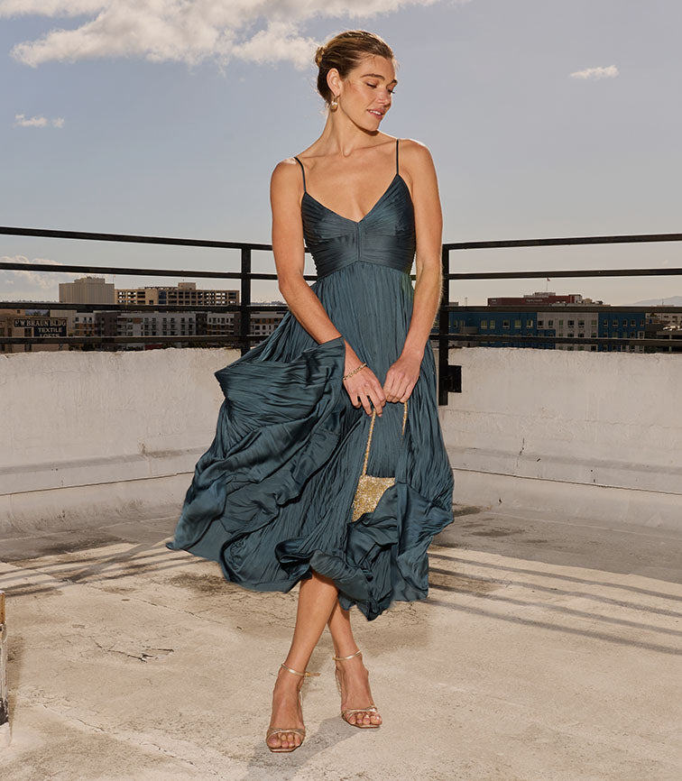 Woman wearing a dark blue sleeveless dress with thin straps and a flowy skirt.