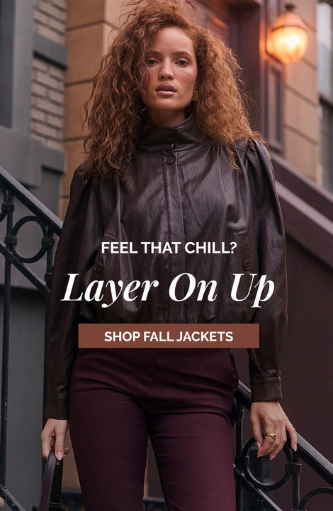 Woman wearing a dark brown leather jacket and maroon pants, standing on a staircase outside.