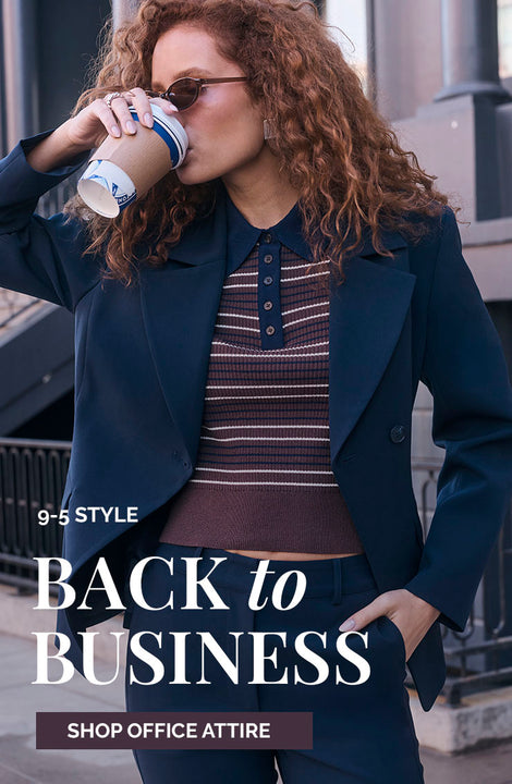 Woman in dark blazer with striped top, drinking coffee outside.