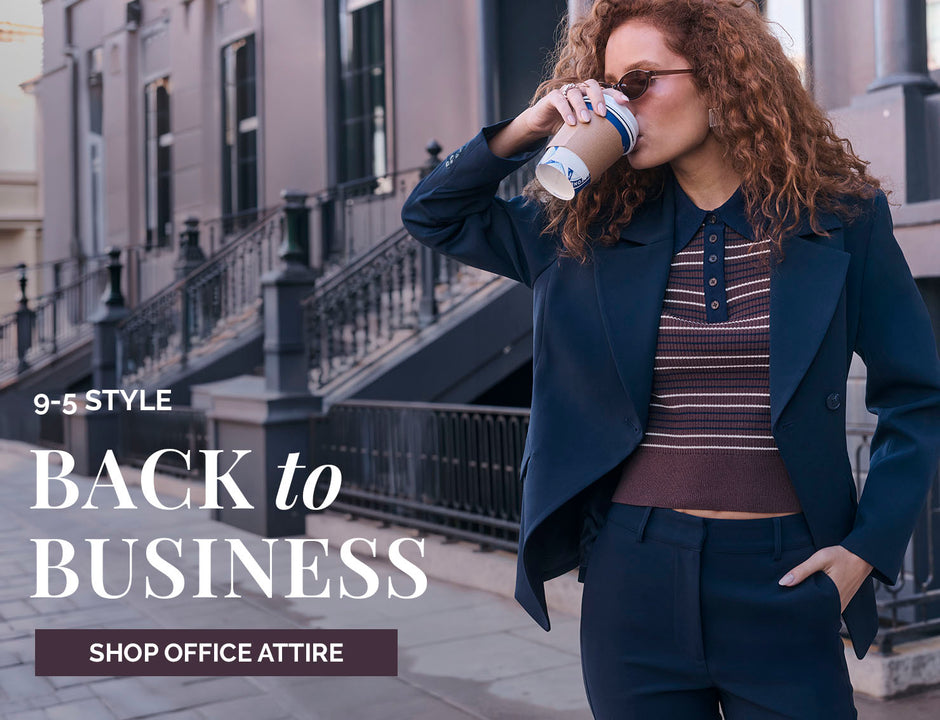 Woman in navy suit with striped top, walking on city street, drinking coffee.