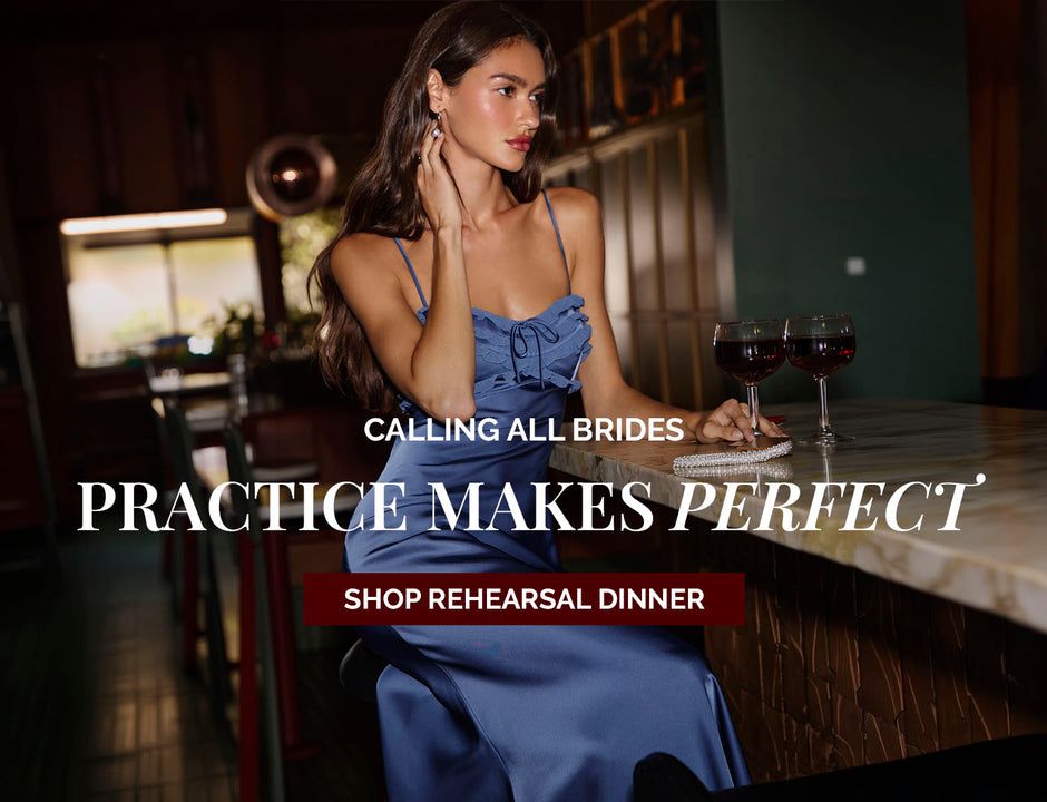 Woman in a blue satin dress with spaghetti straps, sitting at a bar with two glasses of red wine.