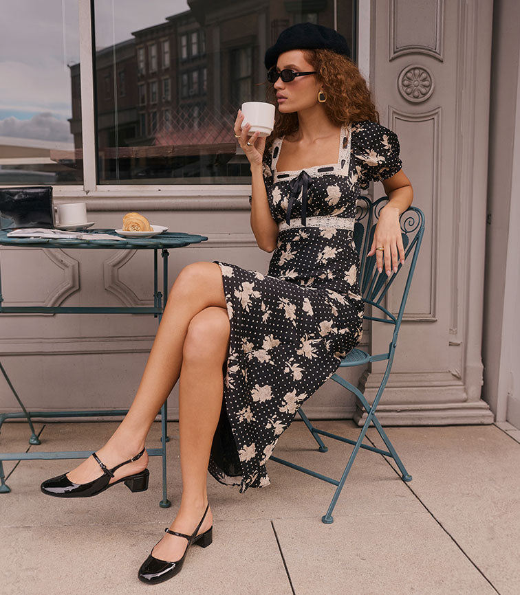 Woman wearing a black dress with white floral and polka dot pattern, black beret, and sunglasses.