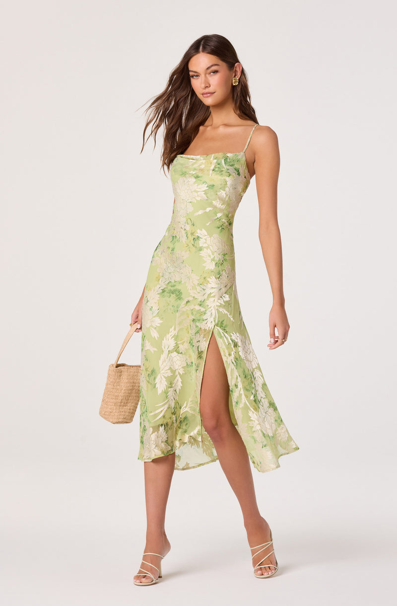 Woman in a light green floral dress with spaghetti straps and a front slit.