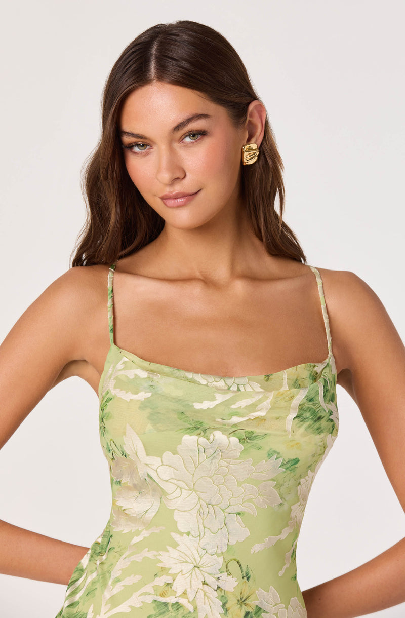Woman in a green floral pattern spaghetti strap dress and gold statement earrings.