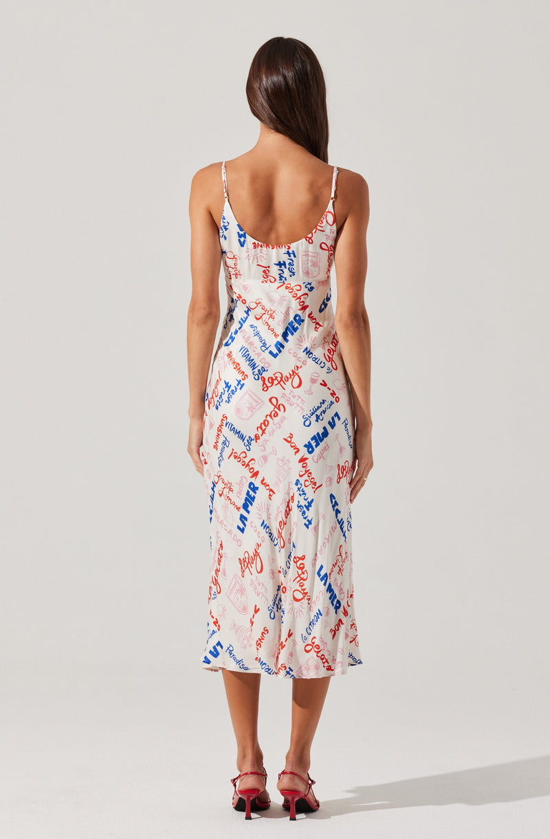 A woman is wearing a sleeveless, spaghetti strap midi dress with a white background. The dress is decorated with various words and phrases in red and blue, arranged in different directions. She is also wearing red high-heeled shoes.