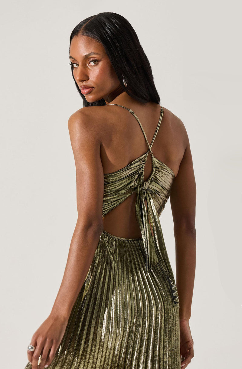 A woman is wearing a shiny, metallic gold and black striped dress with a pleated skirt. The dress has thin spaghetti straps and features a cutout at the back, with fabric gathered and tied in a bow.