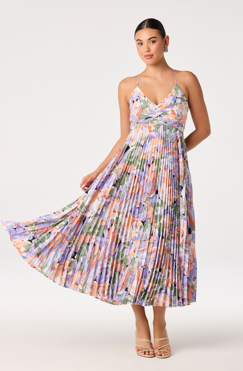 Young woman in a colorful, floral, pleated maxi dress with spaghetti straps.