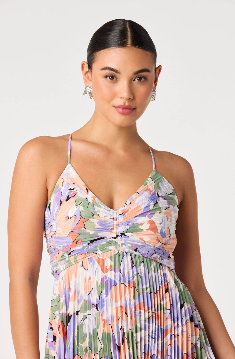 Woman in a colorful, floral-patterned sundress with thin spaghetti straps and pleated skirt.