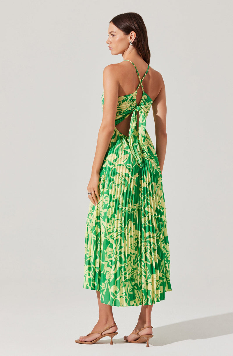 Woman in green and yellow floral dress with cut-out sides and crisscross straps, paired with beige heels.
