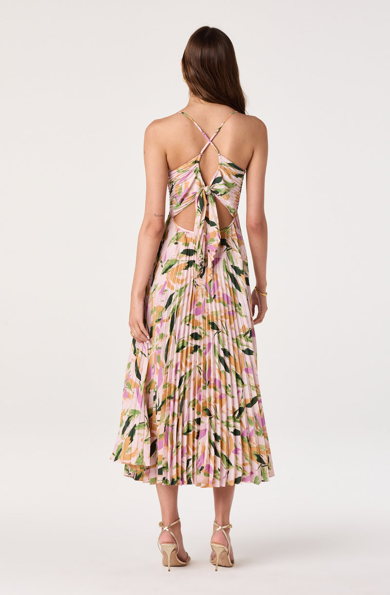 Back view of a woman wearing a sleeveless, floral, pleated dress with a tied waist and crisscross straps.