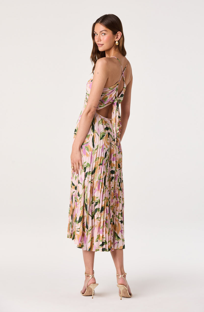 Woman wearing a pink floral pleated dress with spaghetti straps and cutout back.
