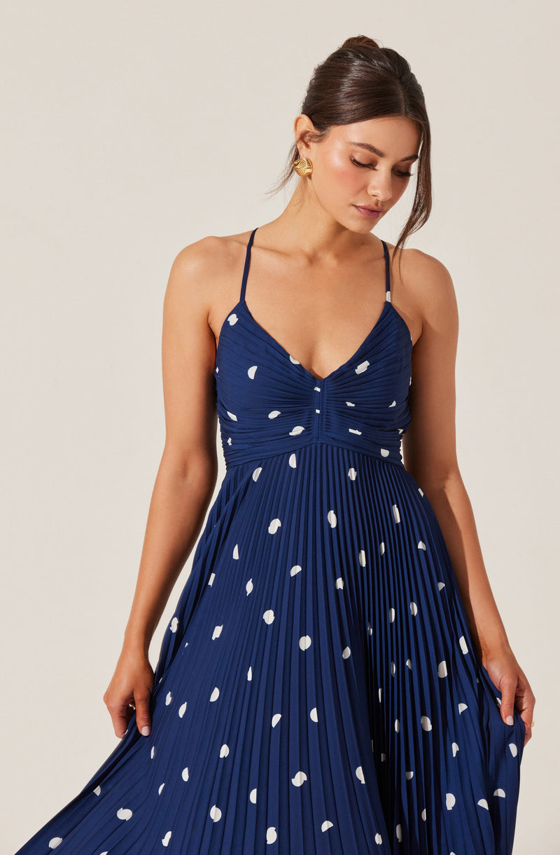 Woman in a navy blue pleated dress with white polka dots and spaghetti straps.