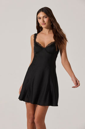 A woman is wearing a black slip dress with lace details along the neckline and straps. The dress has a fitted bodice and a slightly flared skirt that falls above the knees.