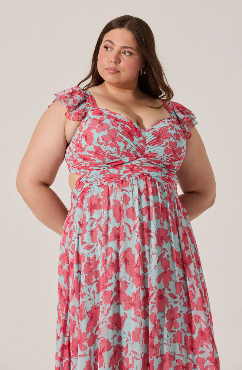 A woman is wearing a light blue dress with a red floral pattern. The dress has ruffled, sheer short sleeves, a sweetheart neckline, and a gathered waistline.