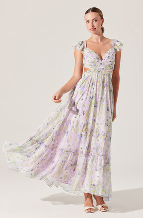 A woman is wearing a flowy, ankle-length dress with a light pastel floral print in shades of purple, green, and yellow. The dress features ruffled sleeves, a sweetheart neckline, and cutout sides. The fabric is lightweight and semi-sheer, giving it an airy, delicate appearance. She is wearing open-toed, high-heeled sandals in an off-white color.