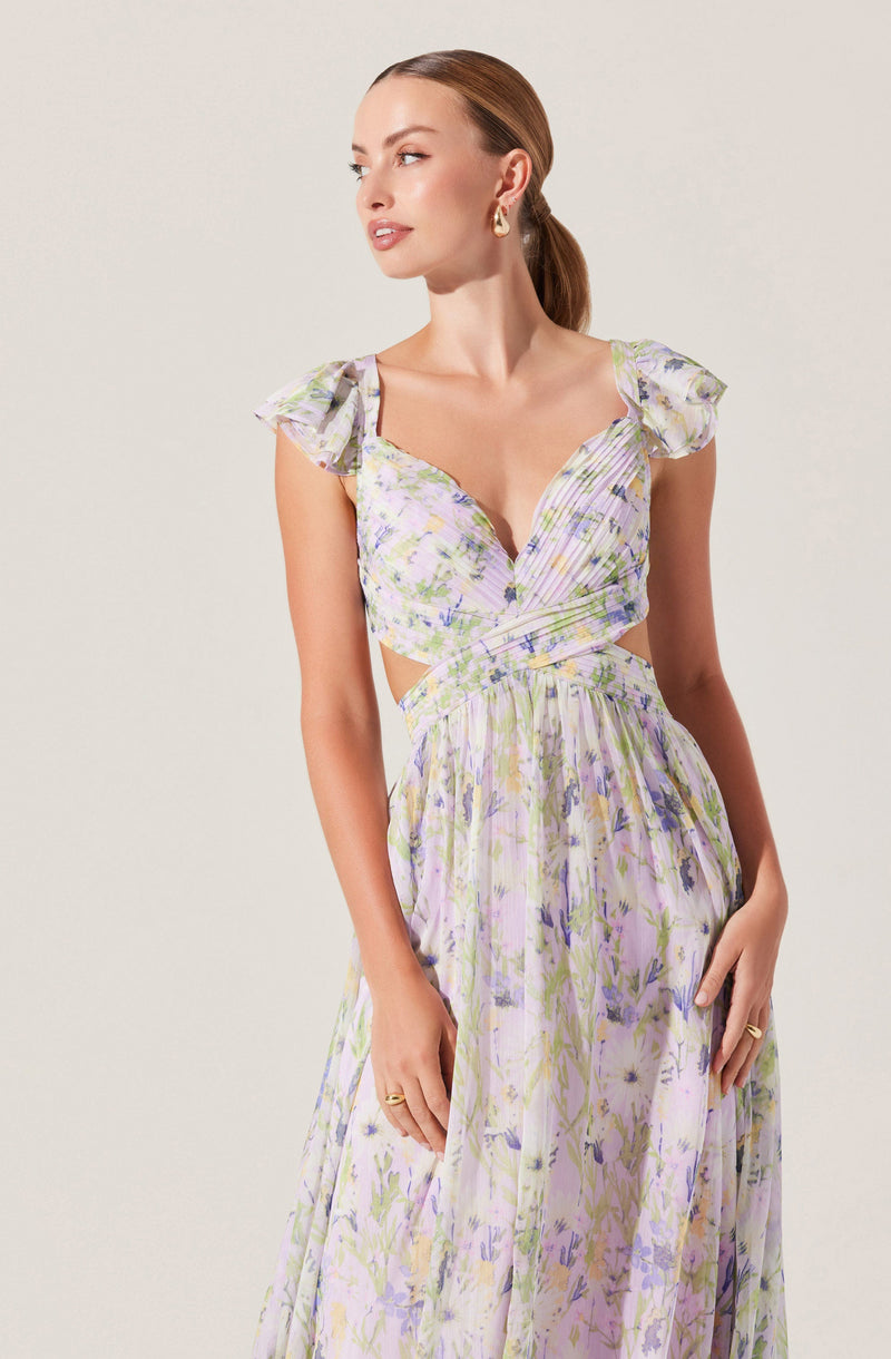 The dress is a floral print with pastel shades of purple, green, and yellow. It features ruffled cap sleeves and a V-neckline with a wrap-style bodice. The waist is slightly cinched, and the long skirt flows down in a light, airy fabric. The overall look is soft, feminine, and elegant.