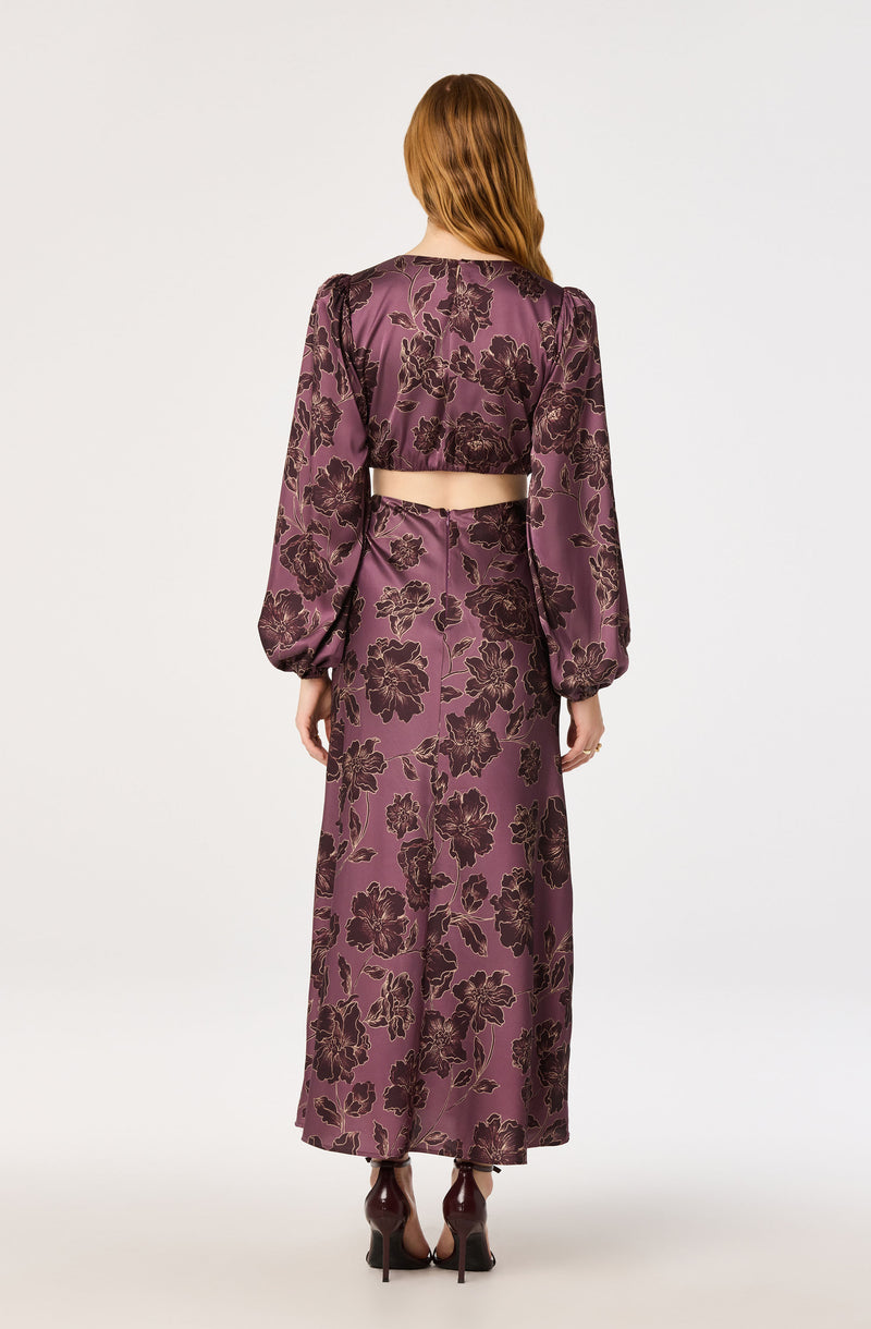 Woman in purple floral satin top and long skirt with puffed sleeves, back view.