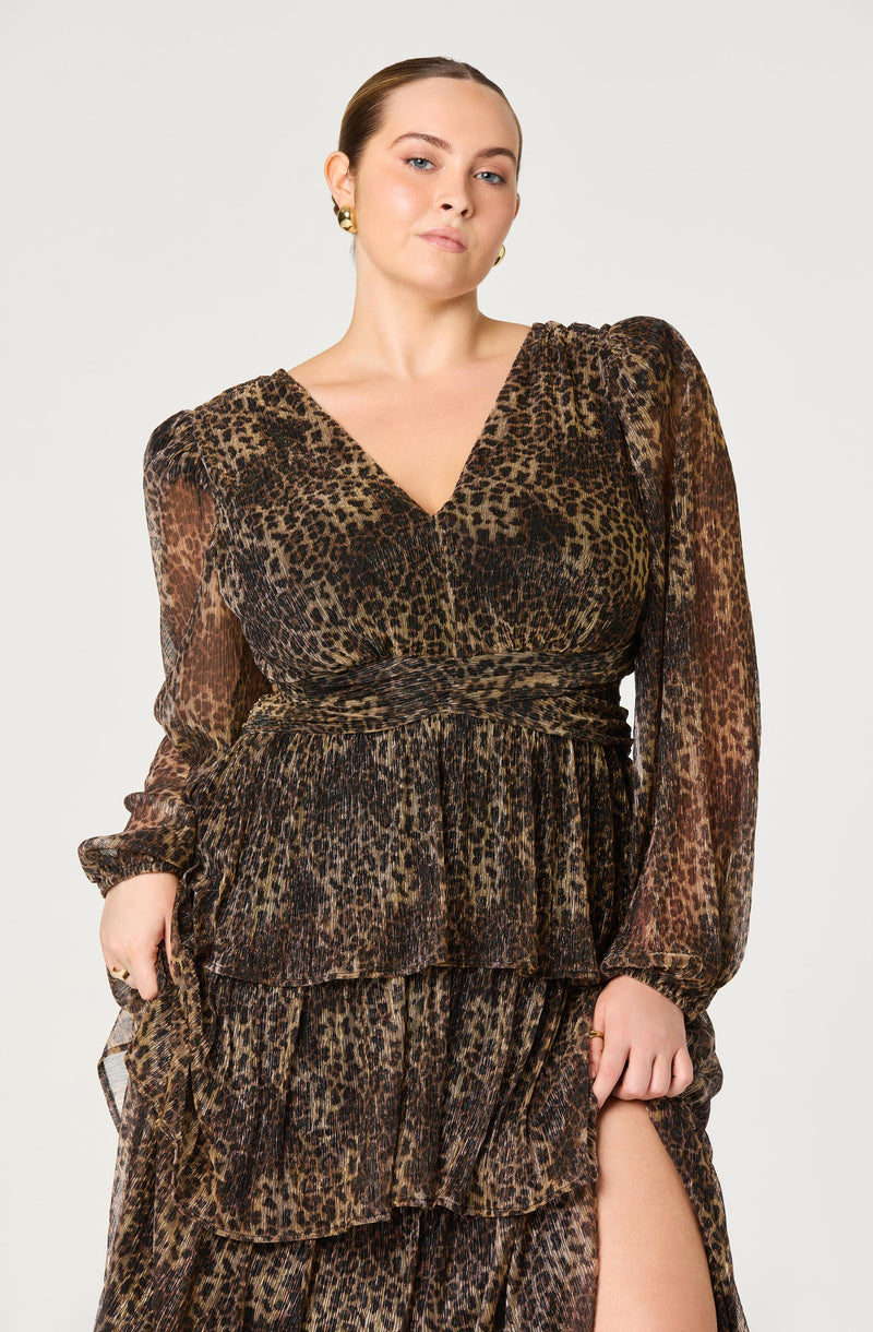 A woman is wearing a long, leopard print dress with a V-neckline. The dress features puffed shoulders, long sheer sleeves, and multiple layered ruffles on the skirt. The fabric appears lightweight and slightly sheer.