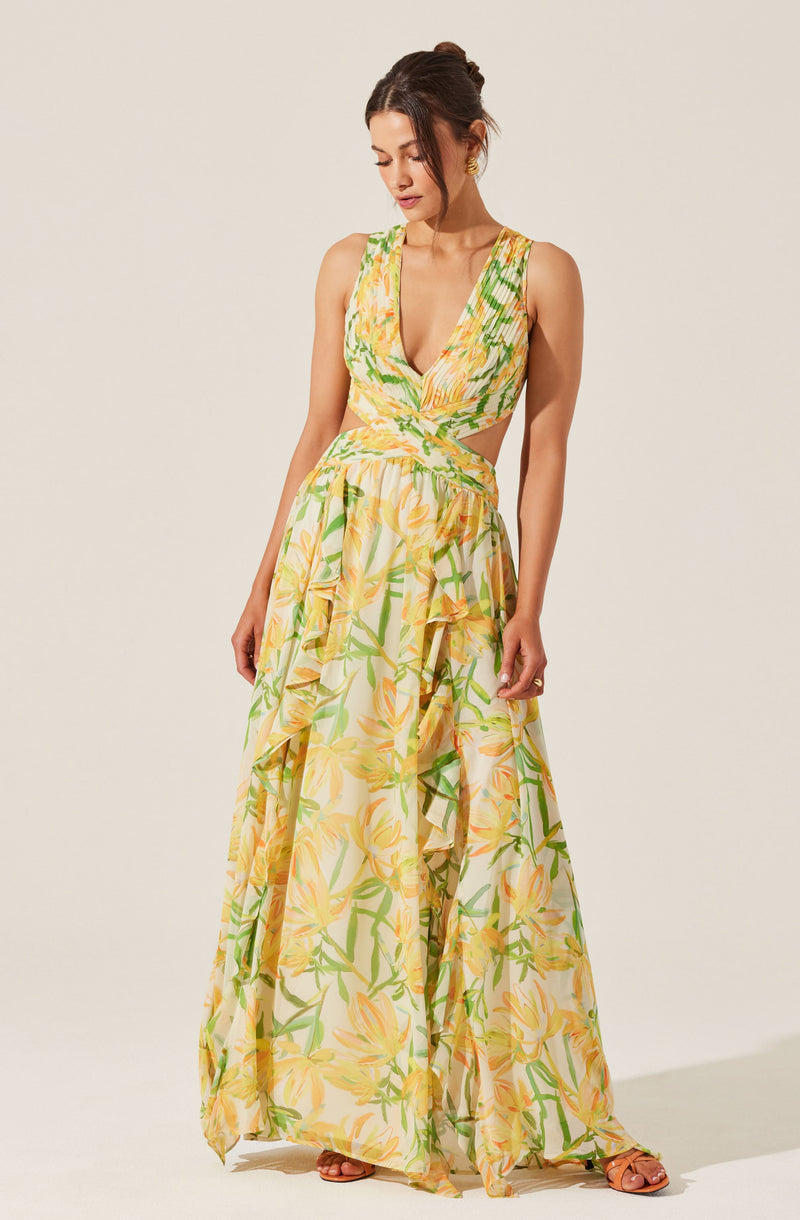 A woman is wearing a sleeveless maxi dress with a deep V-neckline, featuring a vibrant yellow and green floral pattern. The dress has a fitted waist with an overlapping wrap design at the top and ruffle details cascading down the skirt. The fabric appears lightweight and flowy, suitable for warm weather.