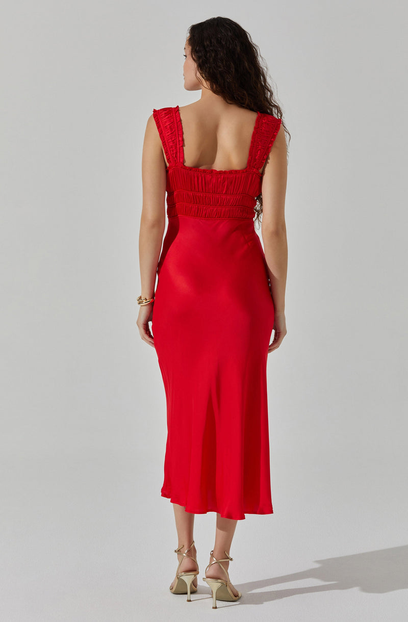 A woman is wearing a fitted, sleeveless red dress with wide, ruffled straps and a gathered, ruched bodice. The dress extends down to mid-calf length and has a flowy skirt. She is wearing nude, strappy high-heeled sandals.