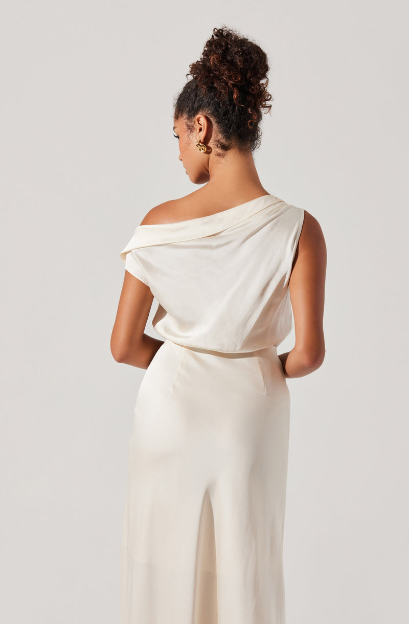 A woman is wearing an elegant off-the-shoulder sleeveless top made of smooth, silky fabric with a draped design. The top is tucked into high-waisted, wide-leg trousers made of a similar smooth fabric, creating a coordinated, sophisticated look in a creamy white color.