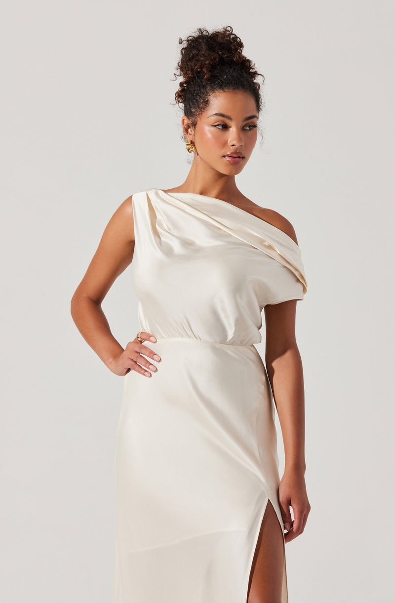 A woman is wearing an elegant off-the-shoulder satin dress in a light cream color. The dress features a draped neckline and a high slit on the side, revealing part of her leg. The fabric has a smooth, shiny finish, giving it a luxurious appearance.
