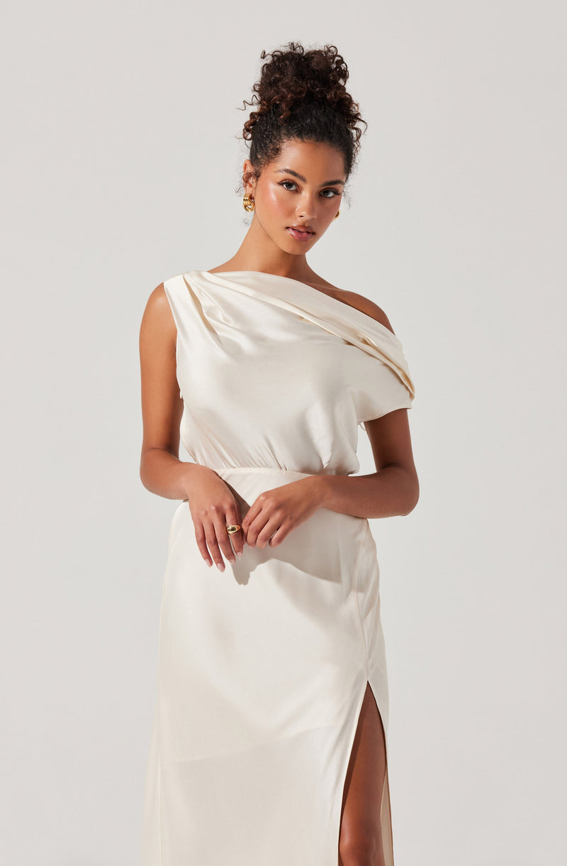 A woman is wearing an elegant, off-the-shoulder, cream-colored satin dress. The dress features draped fabric across the bust and a high slit on the side revealing her leg.